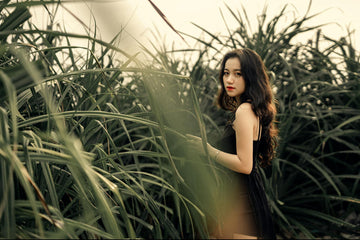 Showcasing charlie's hair and beauty - side view of young asian female in elegant black dress standing in green meadow wit...