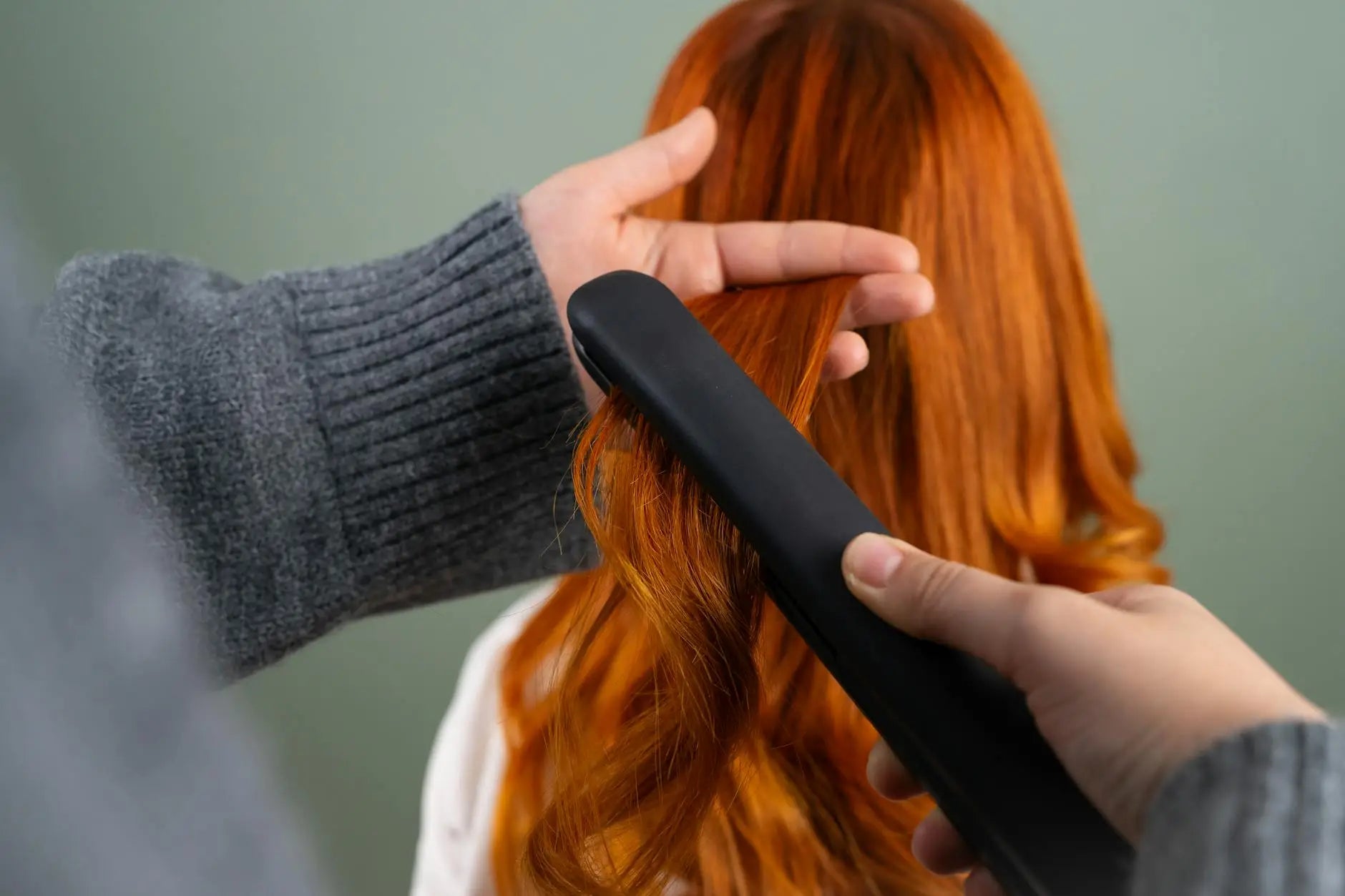 Featuring detangler - hands styling long red hair using a flat iron indoors. haircare and beauty concept. for detangler