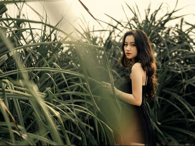 Showcasing charlie's hair and beauty - side view of young asian female in elegant black dress standing in green meadow wit...