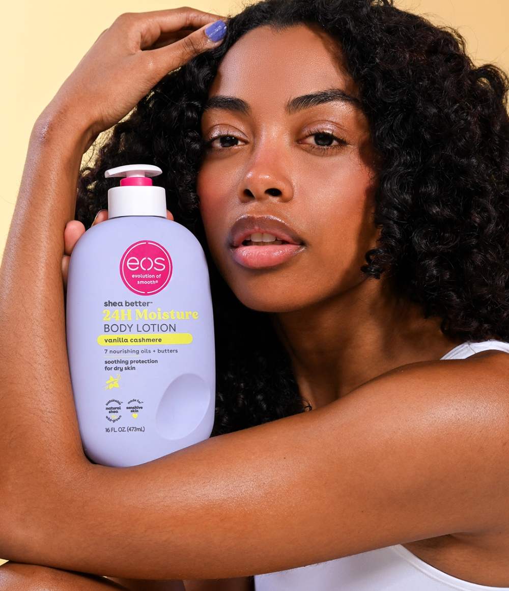 Woman holding an eos body lotion bottle against a beige background
