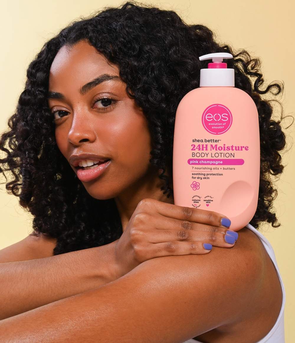 Woman holding a pink bottle of eos 24H Moisture Body Lotion against a beige background