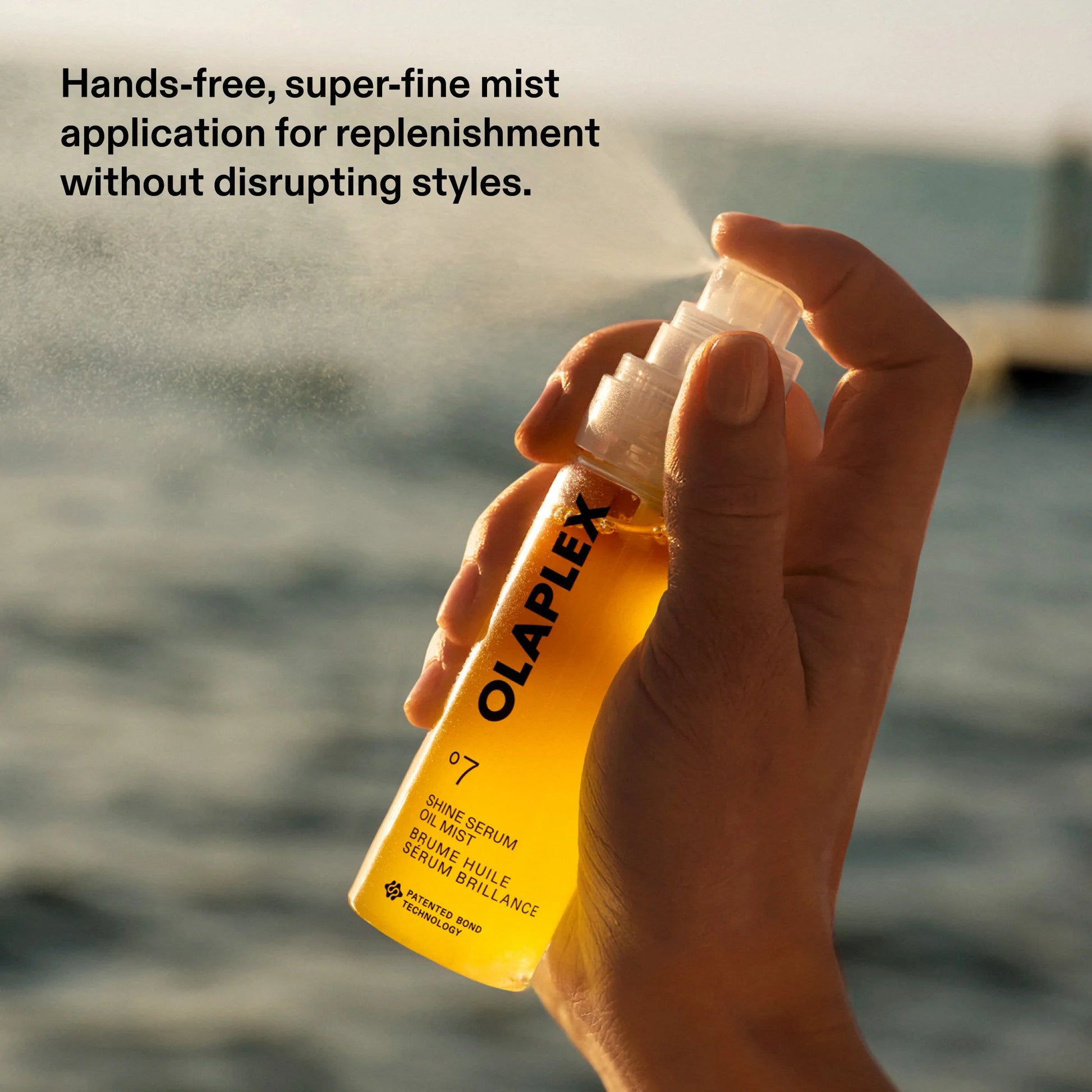 Hand holding Olaplex bottle with mist application against a blurred water background