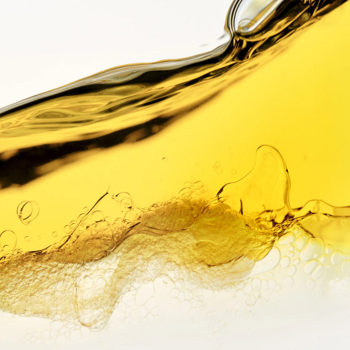 Close-up of flowing yellow liquid with bubbles on a white background