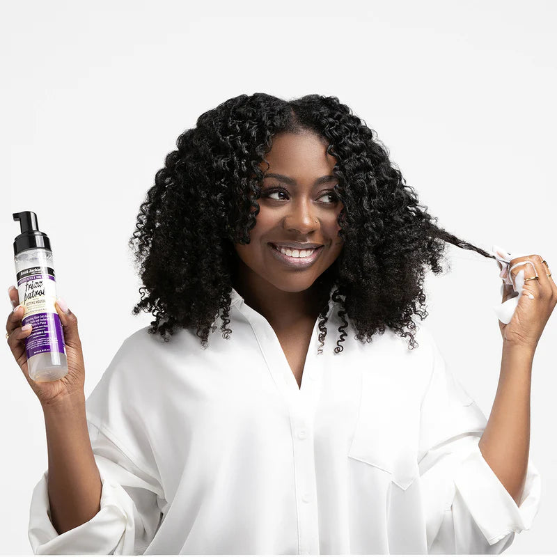 Woman with curly hair holding a bottle of hair product against a white background