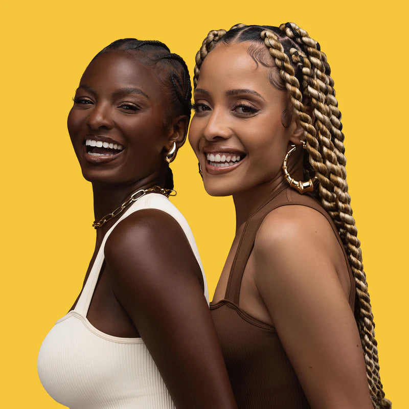 Two women with styled hair smiling against a yellow background