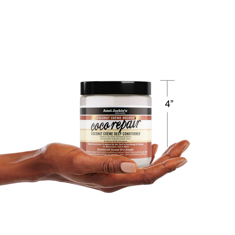 Hand holding a jar of Aunt Jackie's Coconut Creme Deep Conditioner with a measurement label on a white background