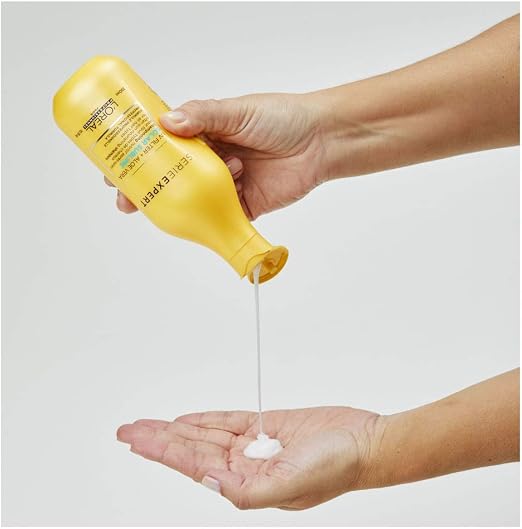 Hand holding a yellow bottle pouring white cream into another hand against a light gray background