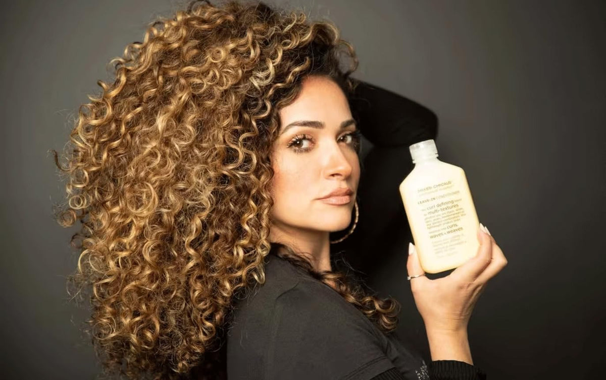 Woman with curly hair holding a bottle of shampoo against a dark background