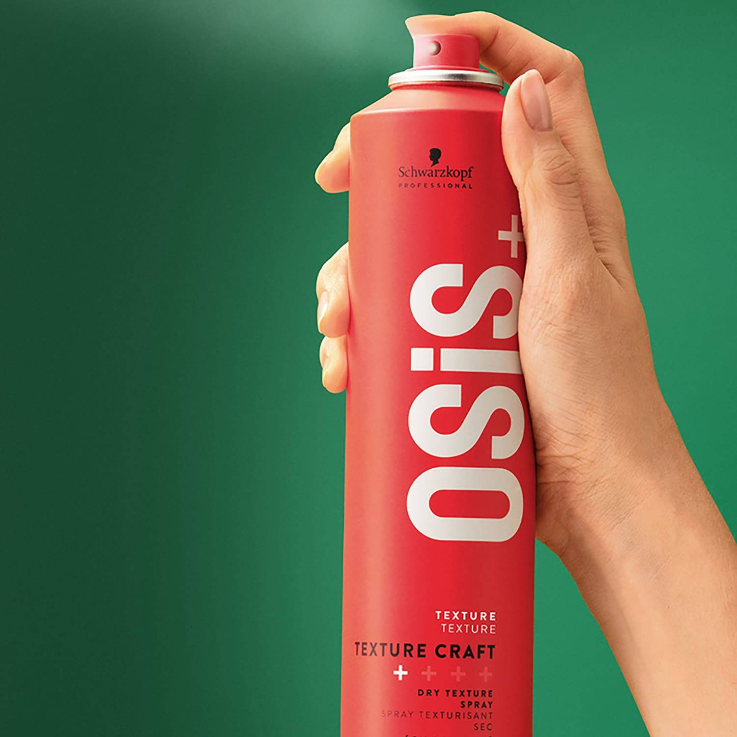 Hand holding a red can of Schwarzkopf OSiS+ Texture Craft spray against a green background