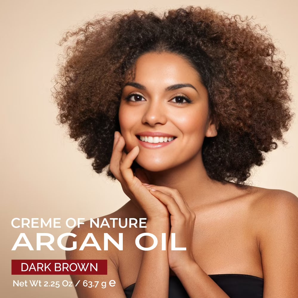 A smiling woman with voluminous dark brown curly hair poses against a warm beige background, with text reading 'CREME OF NATURE ARGAN OIL' and 'DARK BROWN' indicating the product shade.