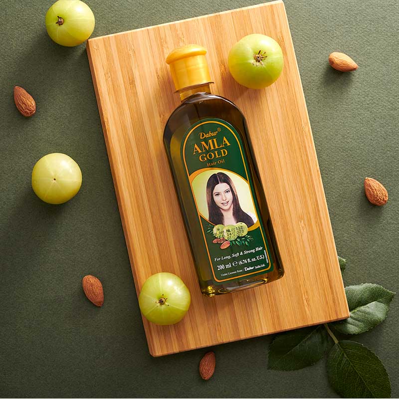 Dabur Amla Gold hair oil bottle on a wooden board with green apples and almonds on a green background