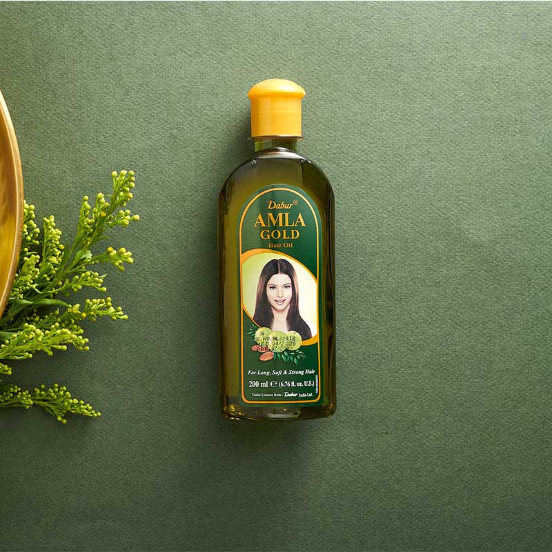 Bottle of Dabur Amla Gold on a green background with green leaves.