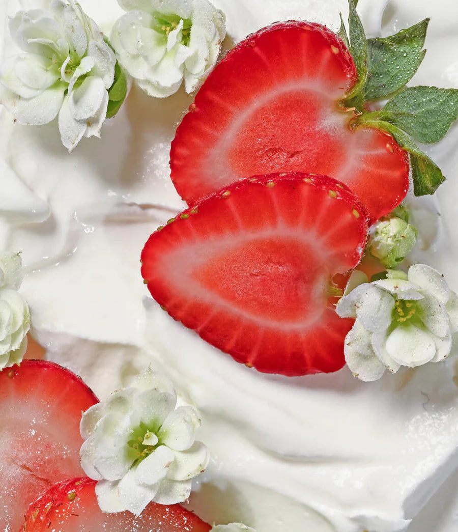 Sliced strawberries and white flowers on a creamy surface