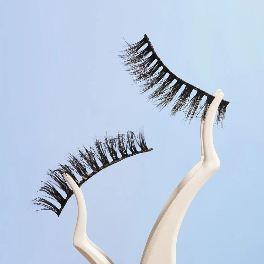 Pair of false eyelashes on a beige holder against a light blue background