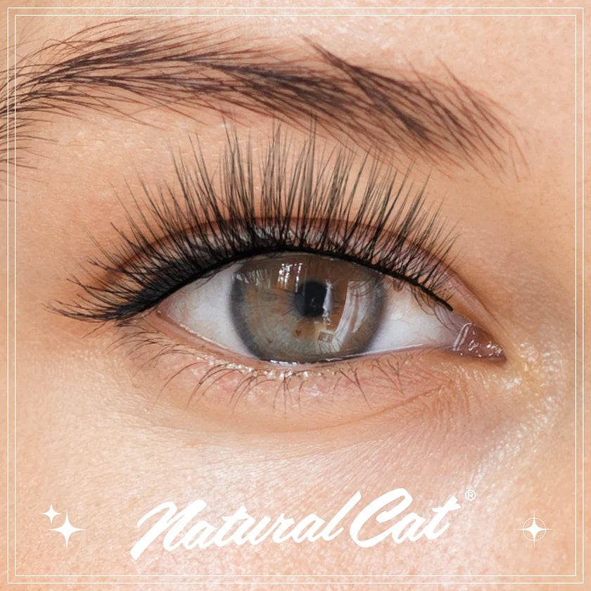 Close-up of a human eye wearing long, dark, curled eyelashes, with visible skin and eyebrow. The brand name NaturalCat appears at the bottom.