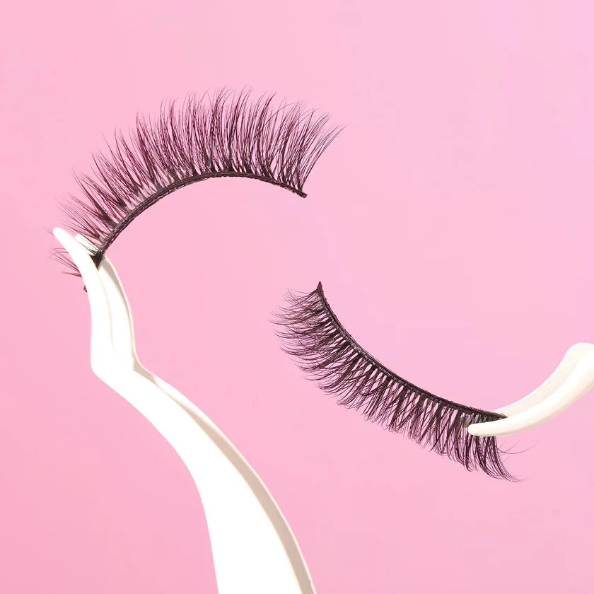 Pair of false eyelashes on a white stand against a pink background