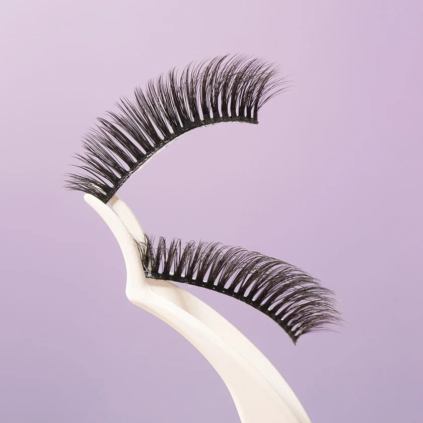 Two pairs of black false eyelashes displayed on a white plastic stand against a solid light purple background.