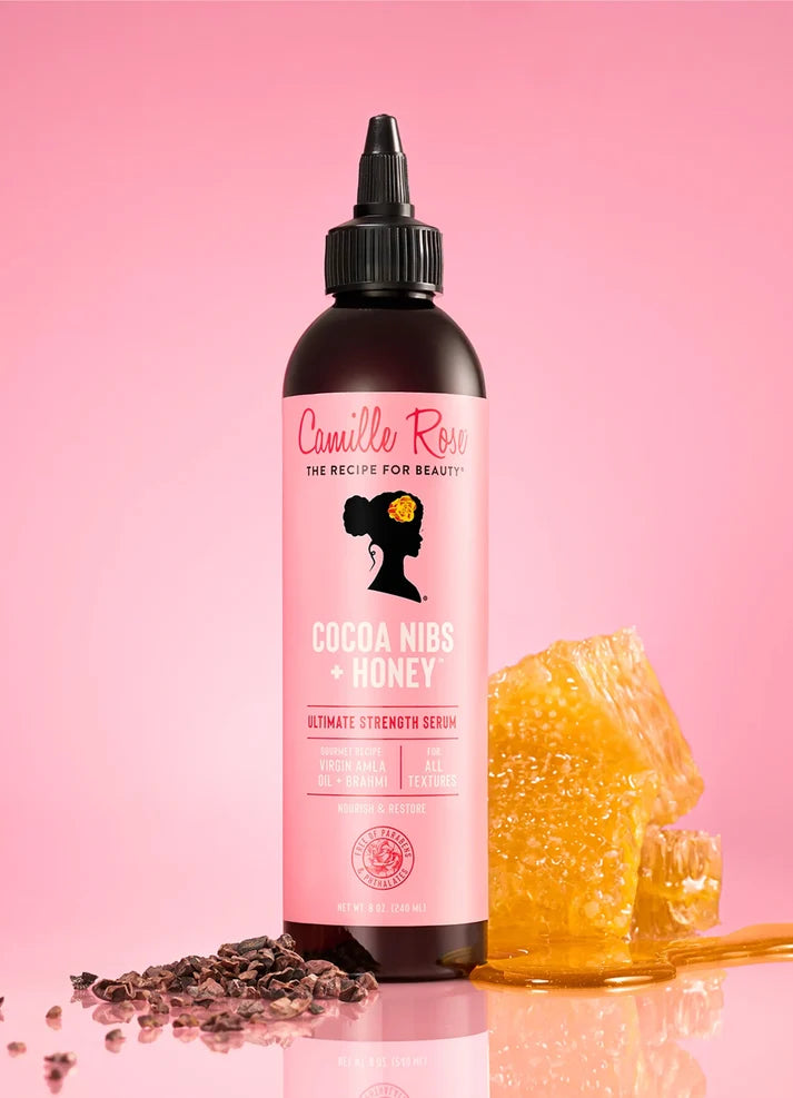 Cosmetic bottle with pink label featuring a silhouette of a woman, surrounded by cocoa nibs and honey on a pink background.