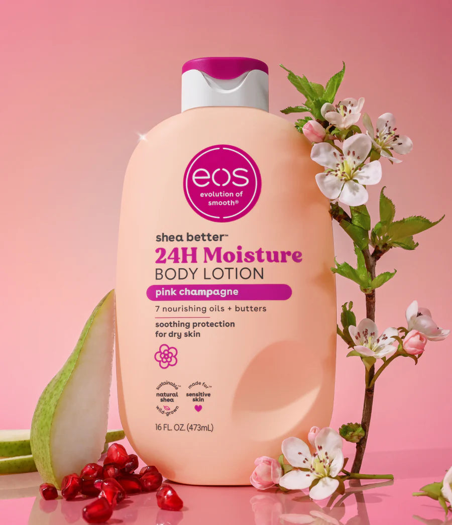 A bottle of EOS 24H Moisture Body Lotion in pink champagne scent, styled with pink cherry blossoms, green leaves, and red pomegranate seeds on a pink background.