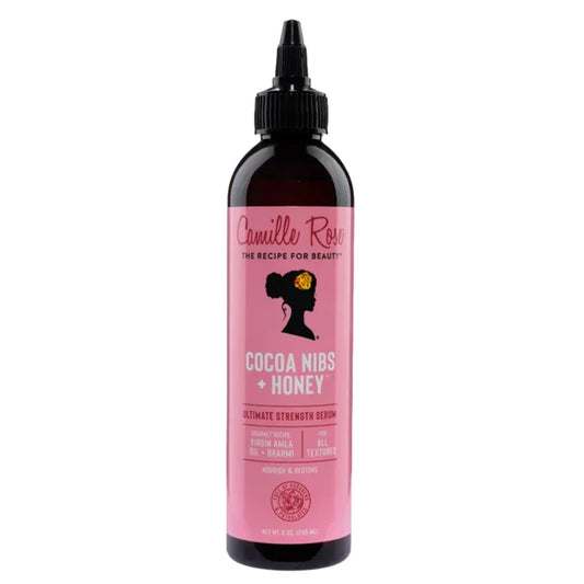 A bottle of Camille Rose Cocoa Nibs + Honey hair serum with a pink label and black cap, shown on a plain white background.