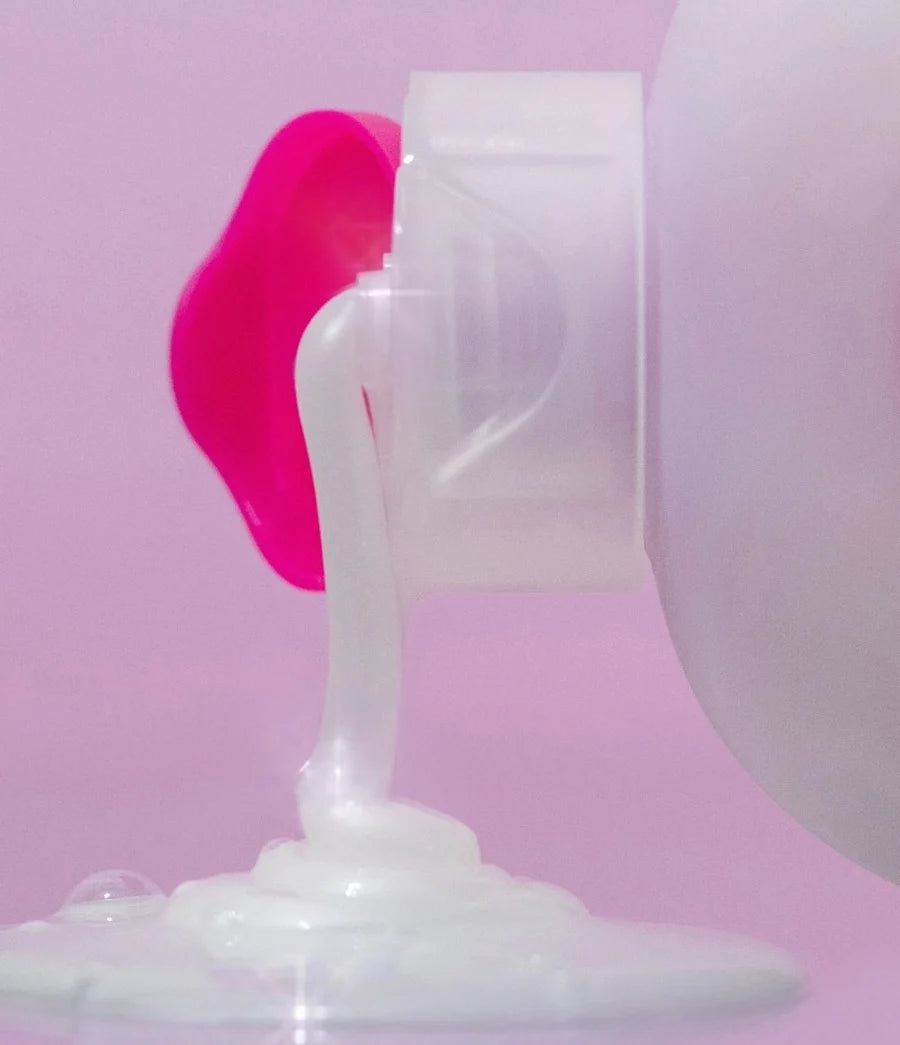 White cream being squeezed out of a pink and white container on a pink background