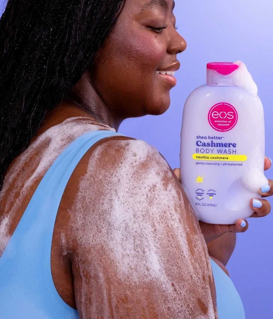 Woman with foamy body wash on her back holding an eos body wash bottle.