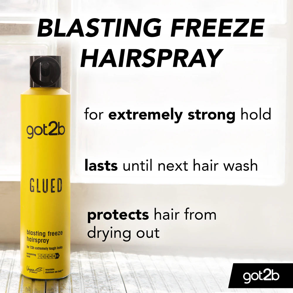 Yellow bottle of got2b Blasting Freeze Hairspray on a light wooden surface with text about its features.