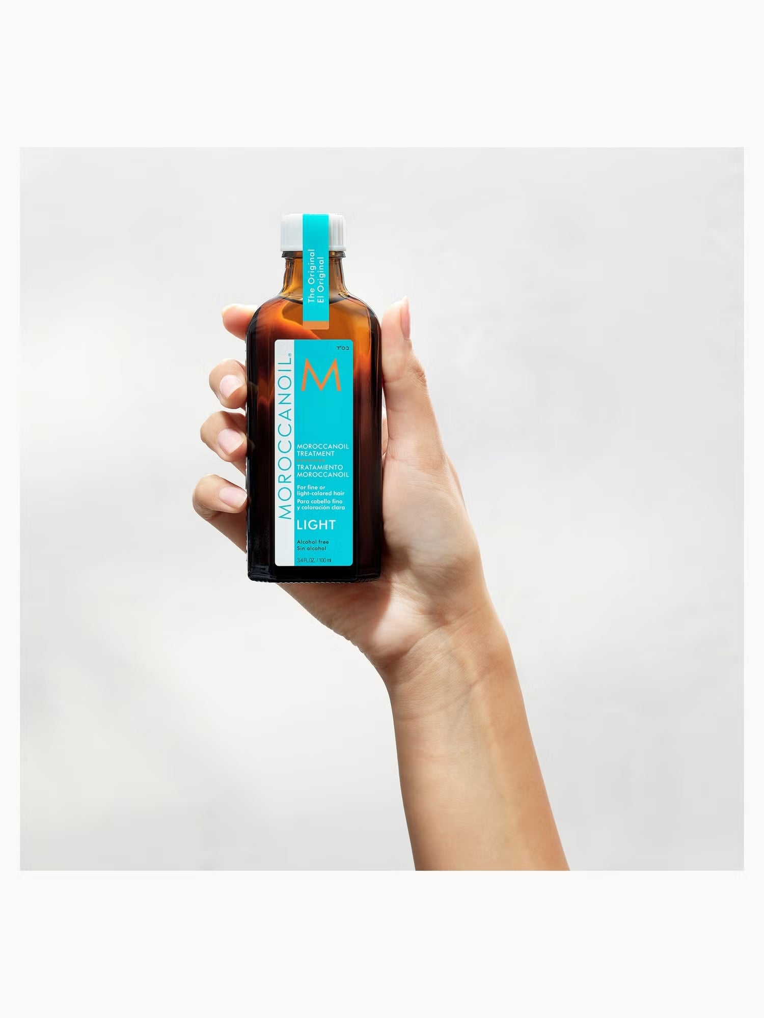 Hand holding a bottle of Moroccanoil product against a white background