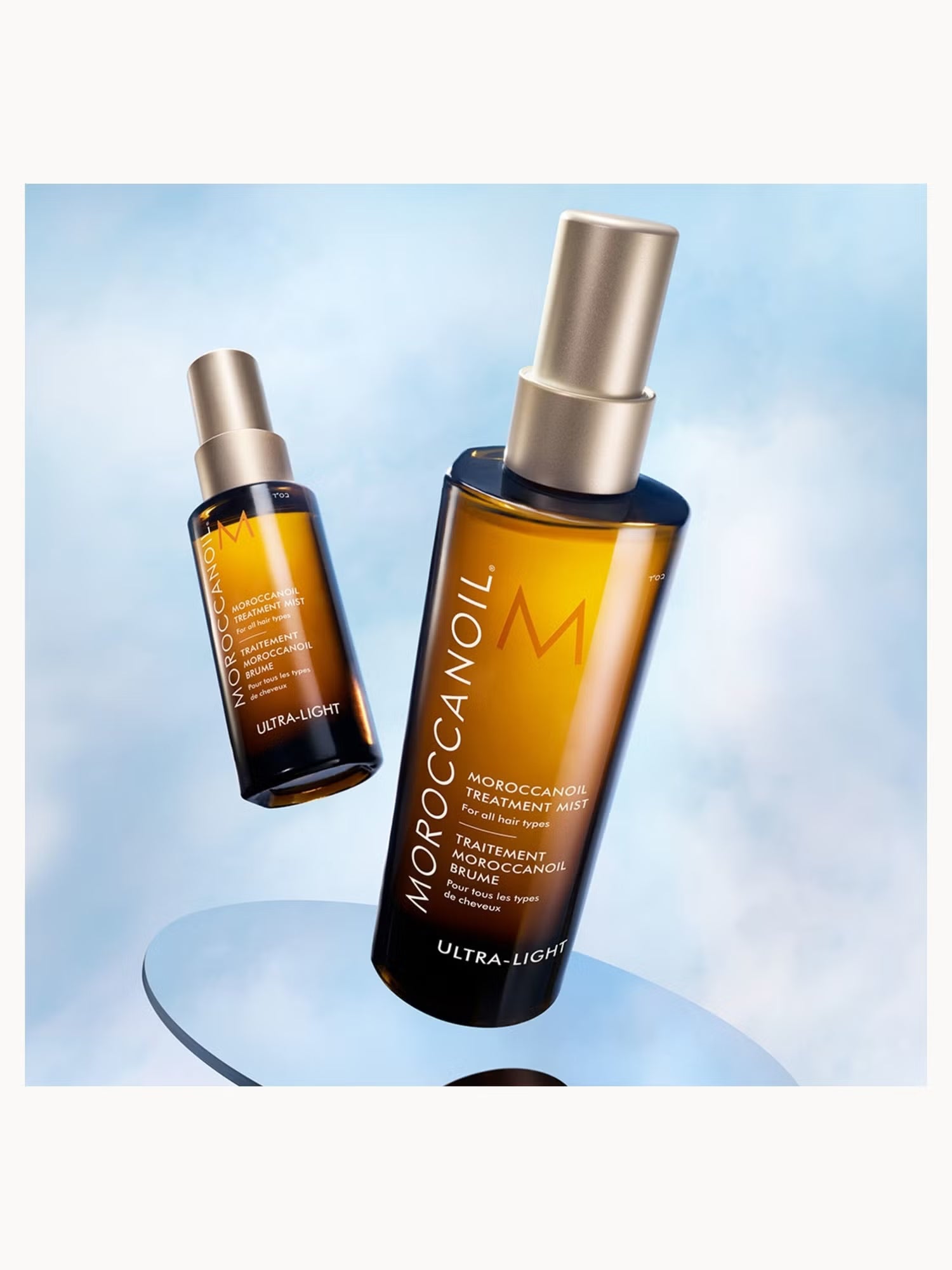 Two bottles of Moroccanoil hair treatment oil on a light blue background