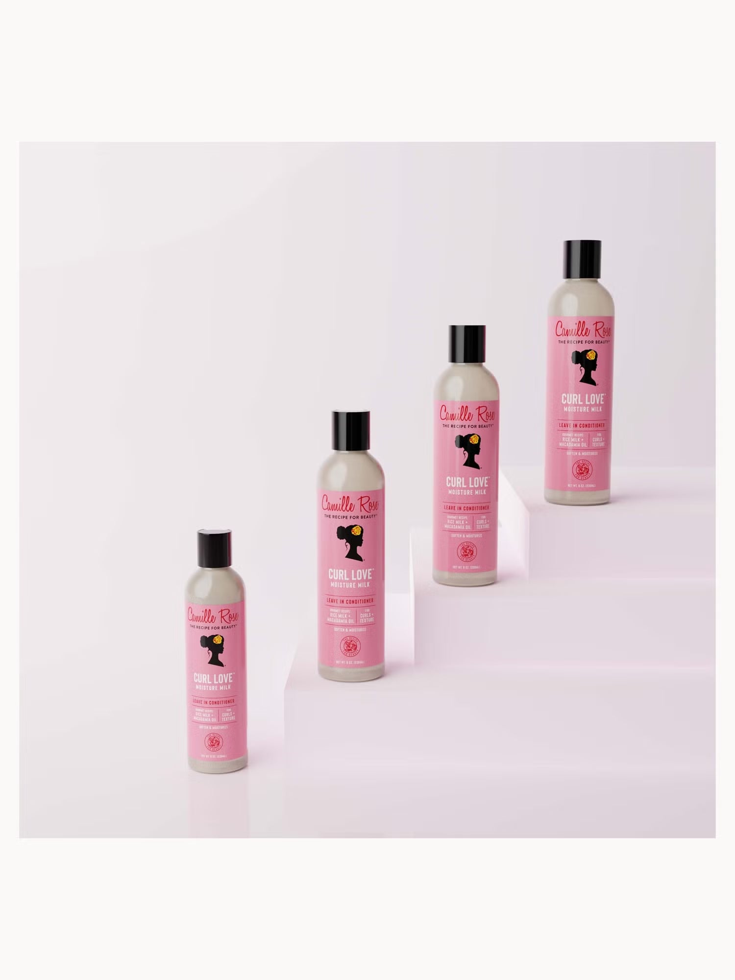 Four bottles of Quatro Feitos Curl Love hair product arranged on white steps against a pale pink studio background.