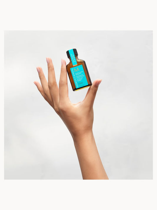 Hand holding a small bottle with a blue label against a light gray background