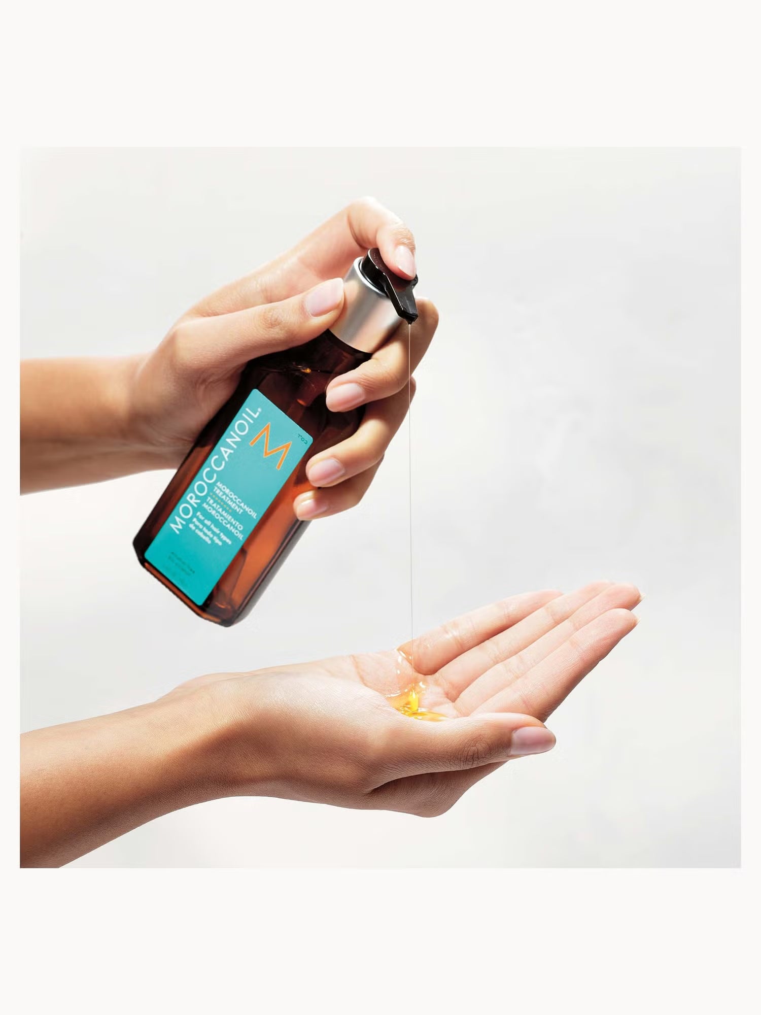 Person holding a bottle of M oil with a white background
