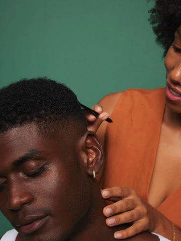 Person applying makeup to another person's ear against a green background