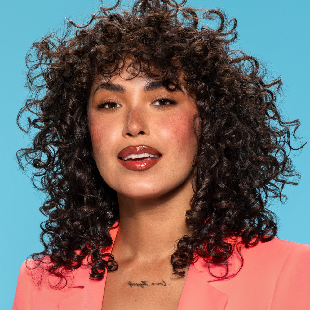Woman with curly hair wearing a pink jacket against a blue background