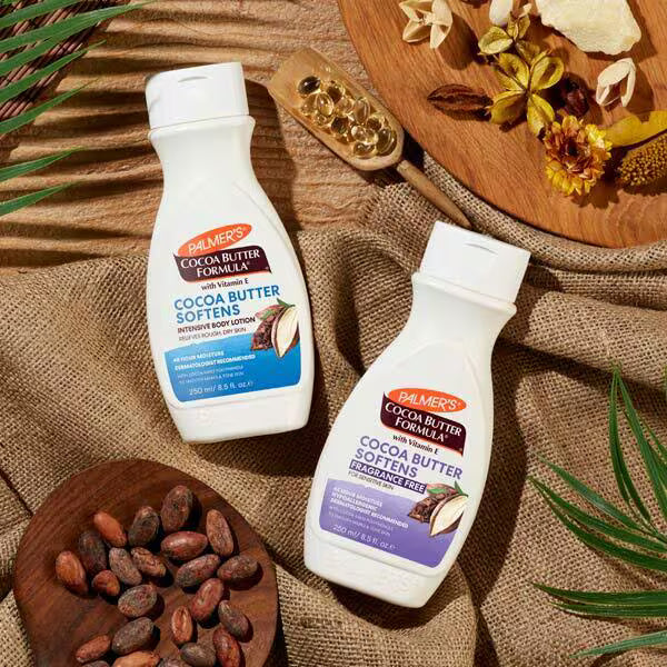 Two bottles of Palmers Cocoa Butter Formula lotion on a textured surface with wooden bowls and cocoa beans.