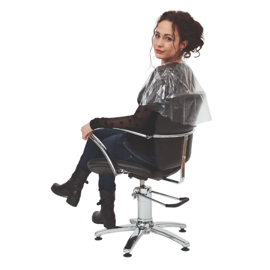 Woman sitting in a salon chair with a clear hairdressing cape on a white background