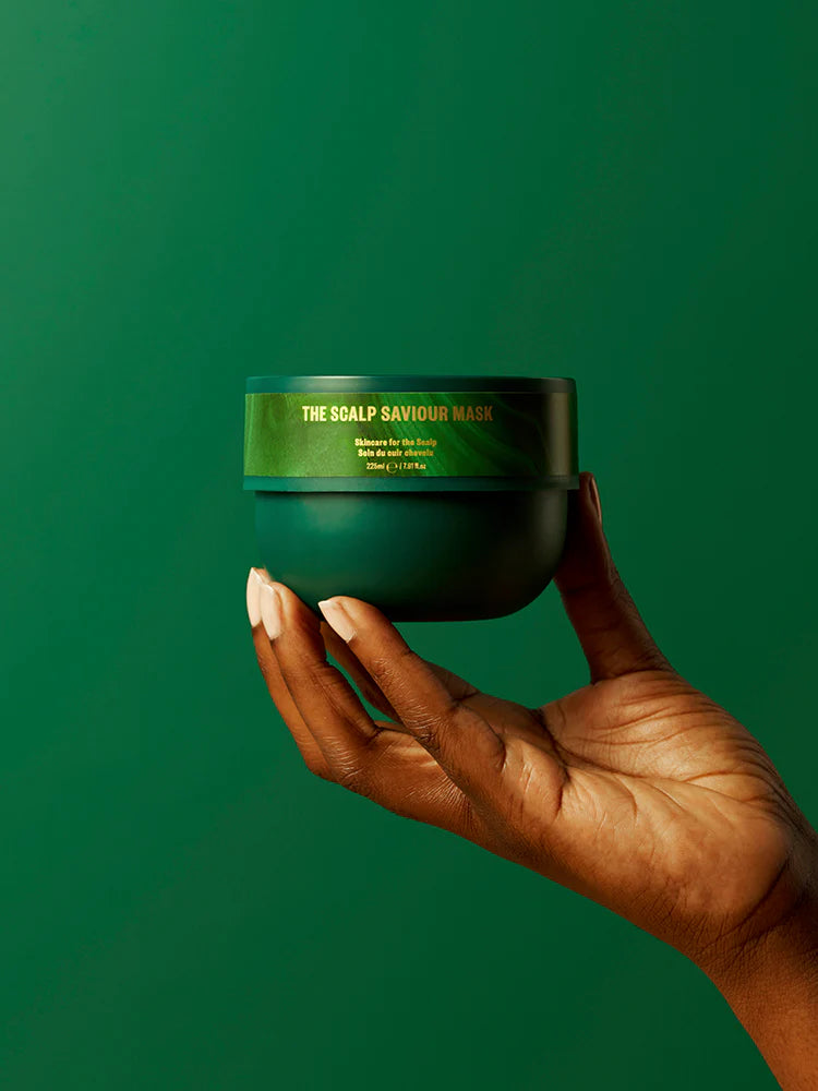 Hand holding a green jar of 'The Scalp Saviour Mask' against a green background
