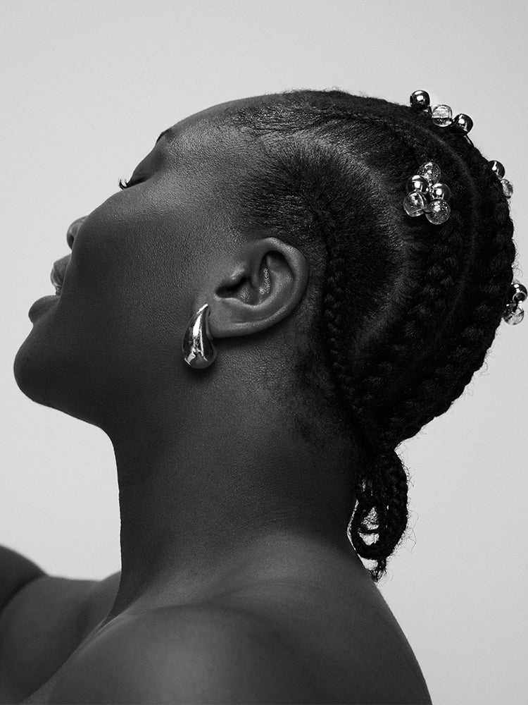 Black and white profile of a woman with braided hair and earrings on a plain background