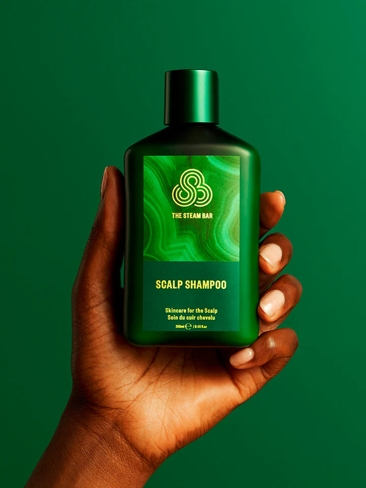 Hand holding a green bottle of scalp shampoo against a green background