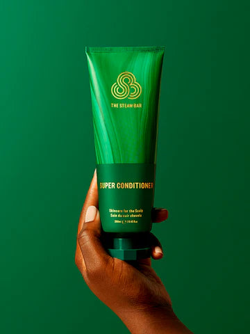 Hand holding a green tube of 'Super Conditioner' against a green background